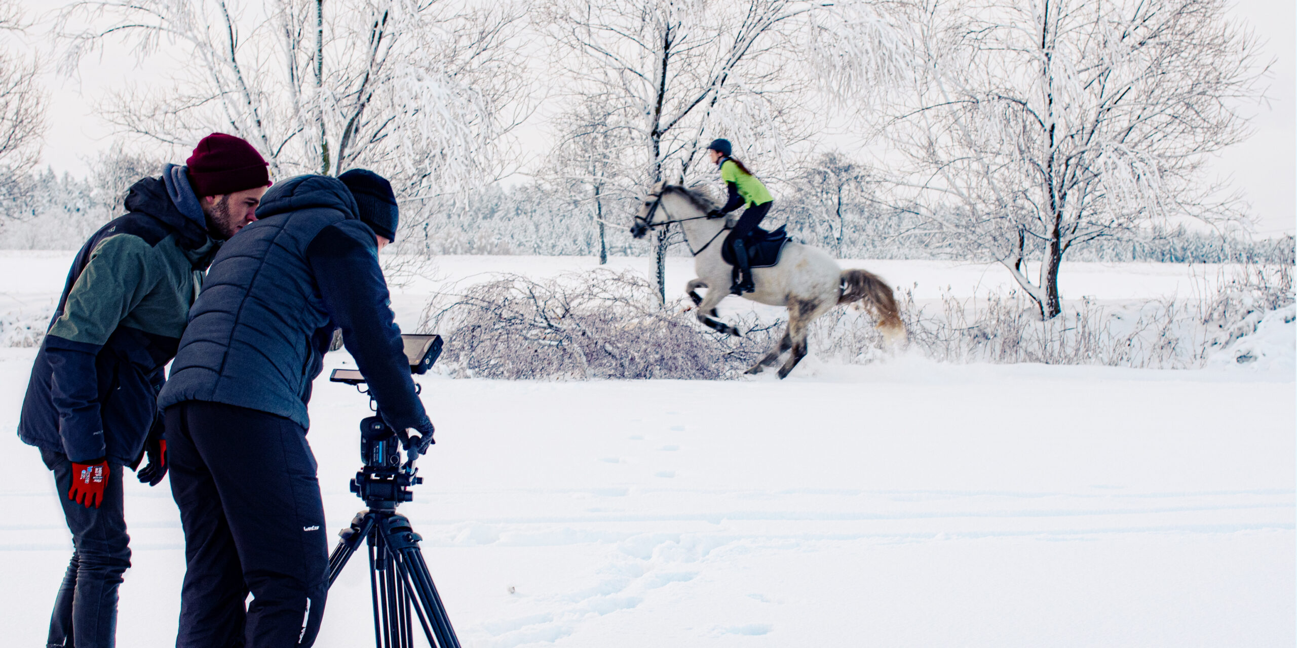 Videodreh im Schnee für die Oralchirurgie Michalik und Richter Limbach-Oberfrohna. Kameramann und Regisseur richten das Bild ein, während im Hintergrund eine Reiterin mit ihrem Pferd galoppiert.