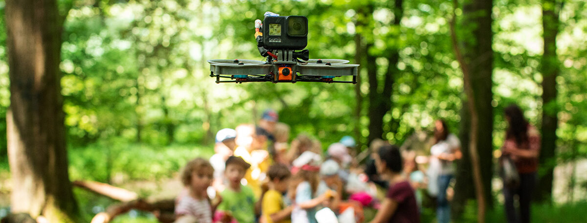 Eine Racing-Drohne, auch FPV Drohne genannt, schwebt über den Köpfen einer Gruppe Kinder