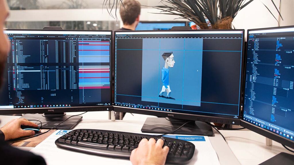 Ein Mitarbeiter von Koschmiederfilm sitzt an einem modernen Arbeitsplatz mit drei Bildschirmen und erstellt Videoanimationen für Chemnitzer Firmen.