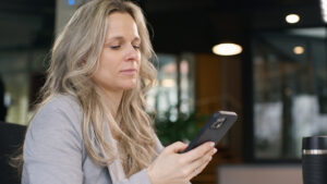 Frau in Büro betrachtet konzentriert ein Smartphone, während sie an einem Tisch sitzt. Optimal für technisches Arbeitsumfeld.